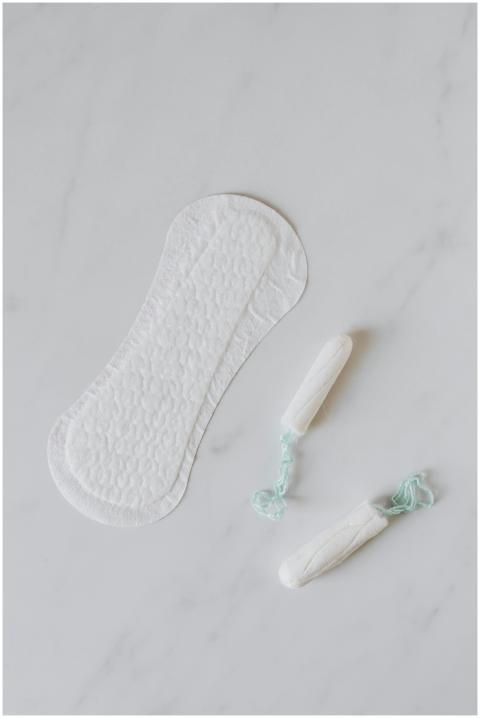 A sanitary pad and tampons on a marble surface, em