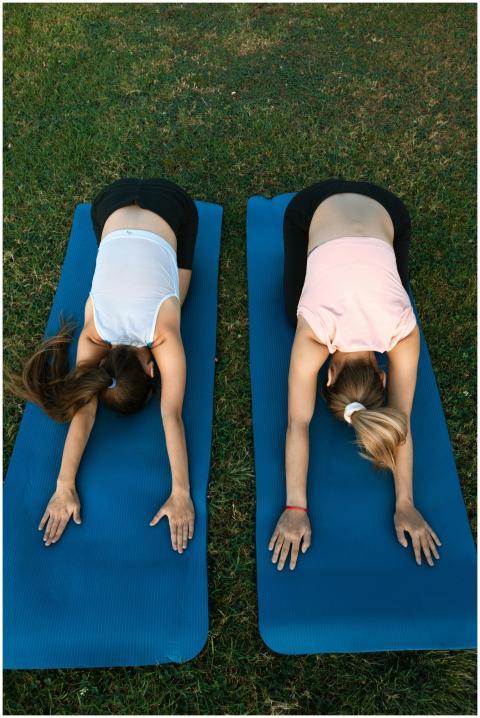 Two women performing yoga poses on mats outdoors,