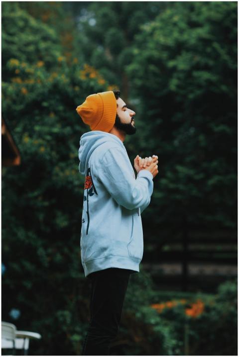 A man in a beanie and hoodie deeply praying outsid