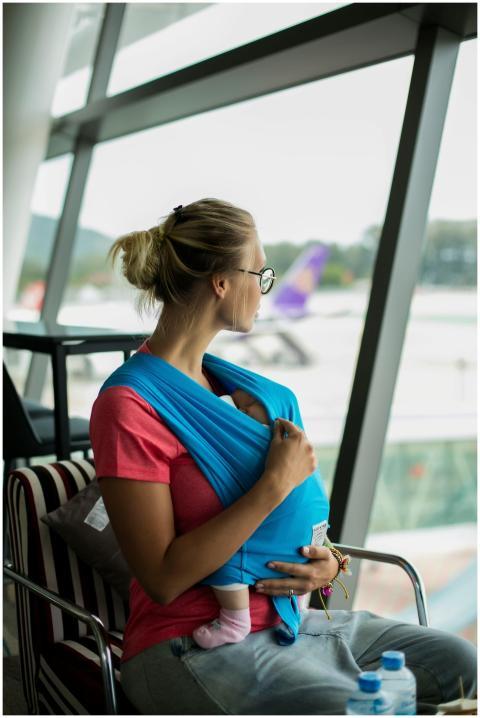 A mother with her baby in a sling looks out the wi