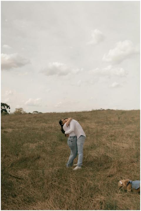 Couple hugging in a grassy field under a cloudy sk