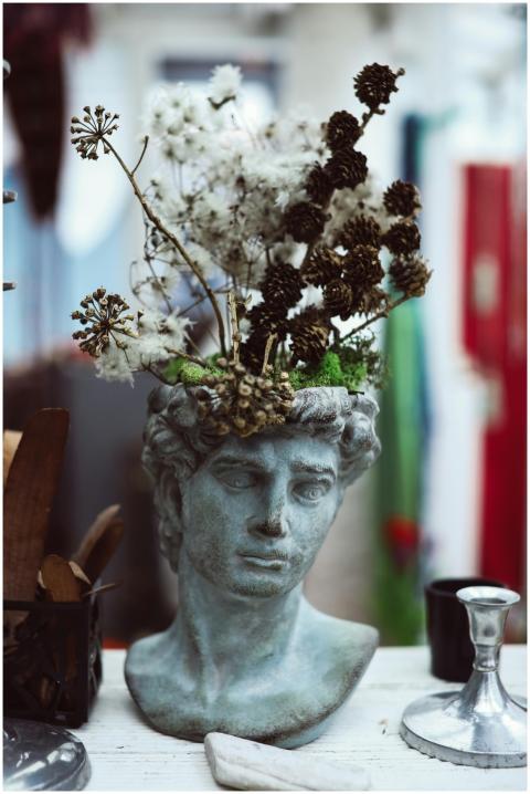 Artistic statue vase with dried flowers on a white