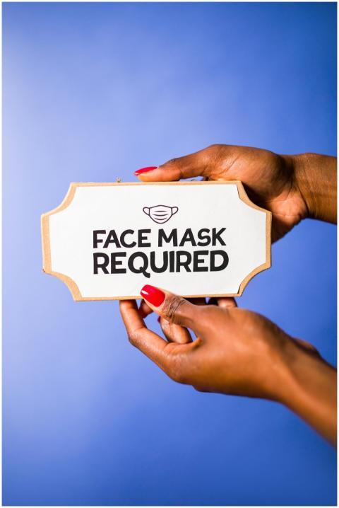 Close-up hands holding face mask required sign on