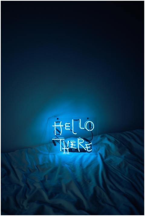 Blue neon sign reading 'Hello There' on a bed, cre