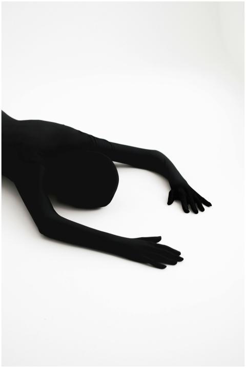 A black-clad figure in a zentai suit lies in an ar