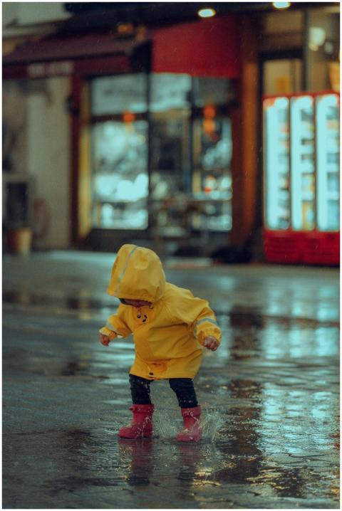 A young child in a yellow raincoat joyfully jumps