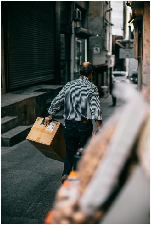 A man carrying a box strolls down a narrow street