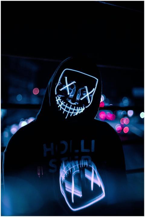 A person wearing a glowing neon mask with a hoodie