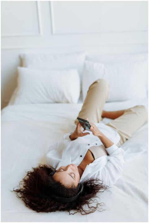 Woman lying on bed in casual clothes, using smartp
