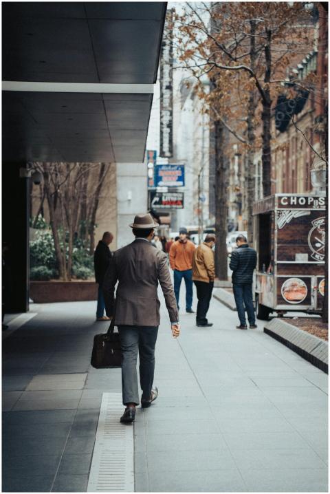 Man in a hat walking along a city street with a su