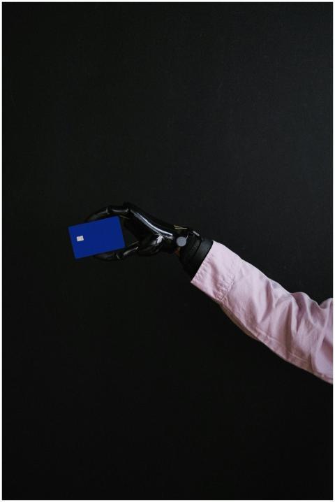 A prosthetic hand holding a bank card against a bl