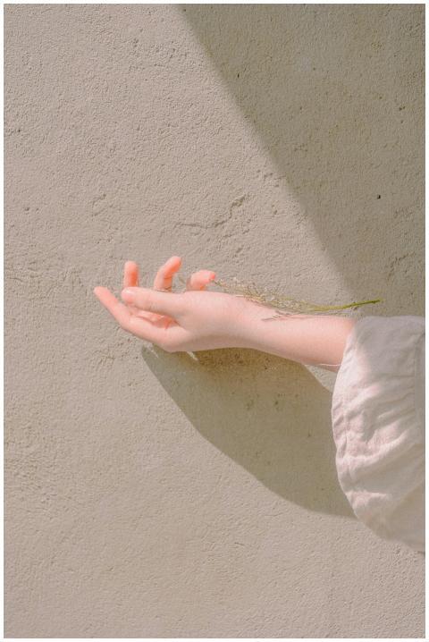 A delicate hand extends towards a sunlit wall, cap