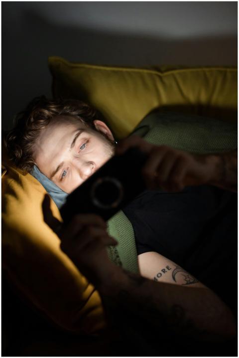 A young man with a beard lies on a couch gaming on