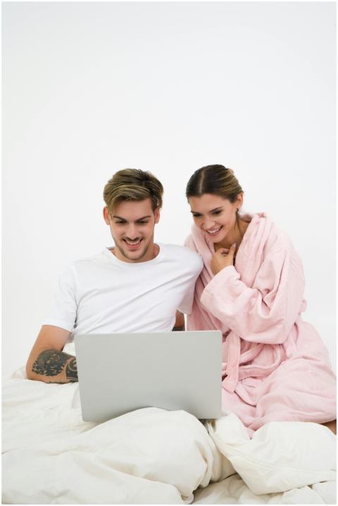 A happy young couple in bed streaming content on a