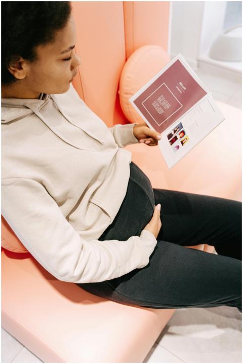 A pregnant woman sits comfortably indoors reading