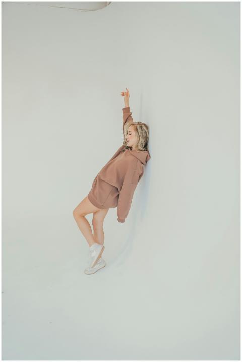 Stylish woman poses in a brown hoodie against a wh