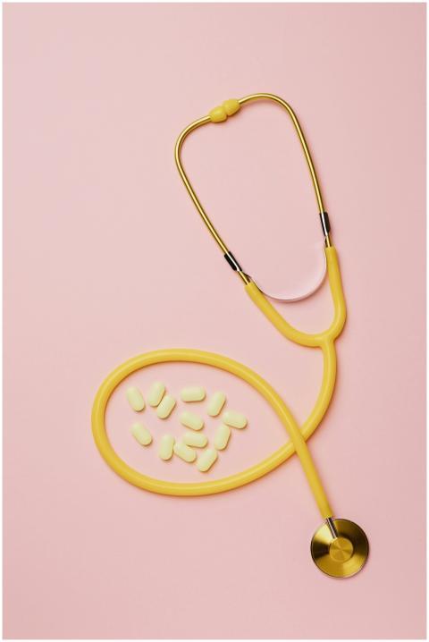 Yellow stethoscope and pills on a pink background,