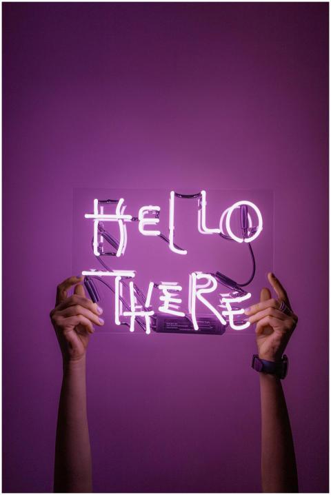 Bright neon sign saying 'Hello There' held by hand