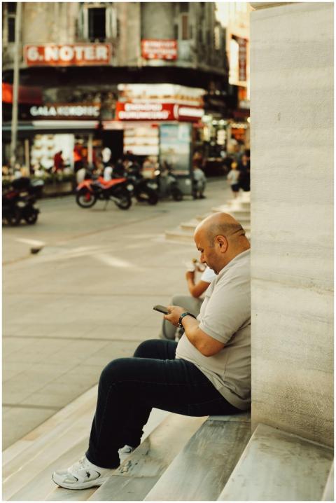 Bald man using phone on steps in bustling İstanbul