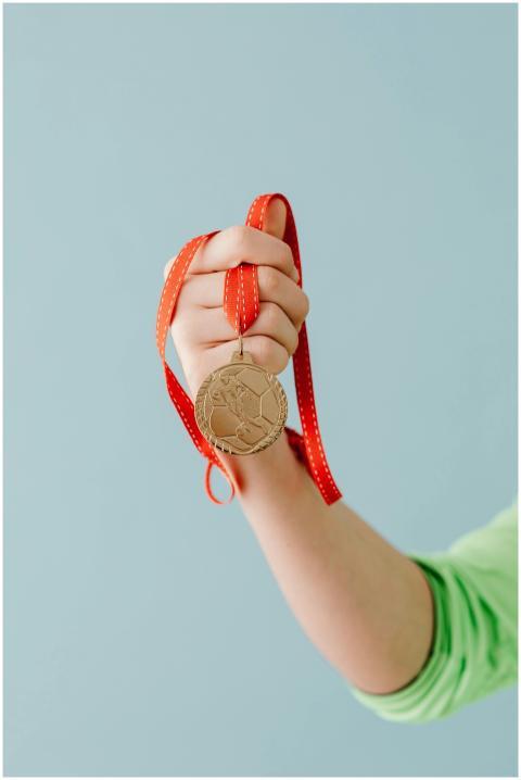 A close-up of a hand holding a gold medal with a r