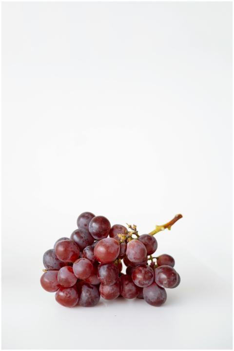 A cluster of red grapes on a white background, per