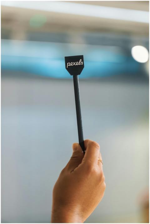 A hand holding a small sign with 'pexels' text, bl