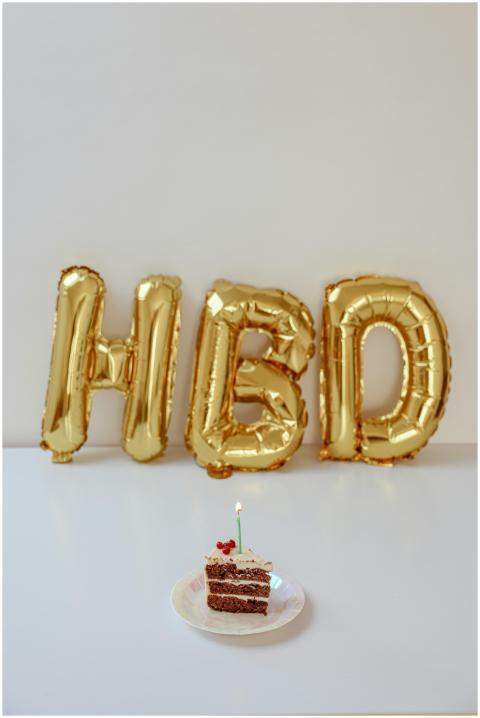 Slice of cake with lit candle and gold HBD balloon