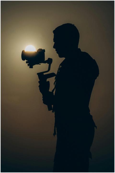 Silhouette of a person filming with a camera at su