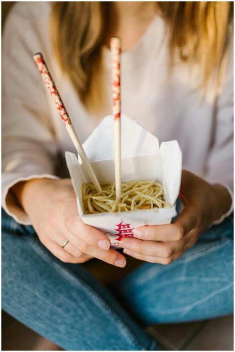 A woman holding a takeout box of noodles with chop