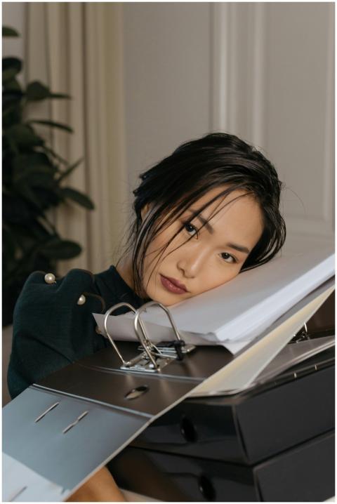 Asian woman resting on a stack of office folders,