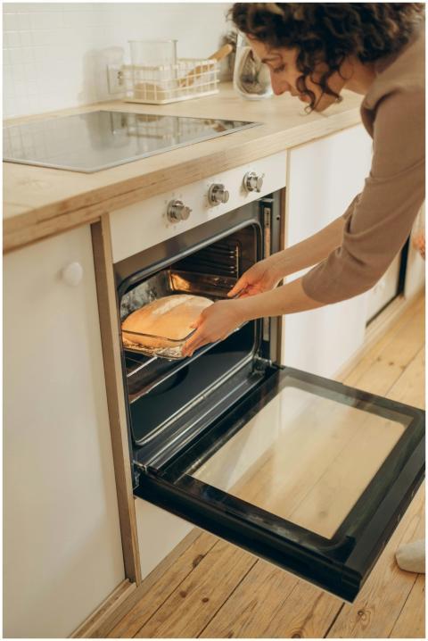 Adult woman placing bread in oven, showcasing home