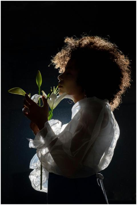 A woman in sheer clothing holds lilies in a dramat