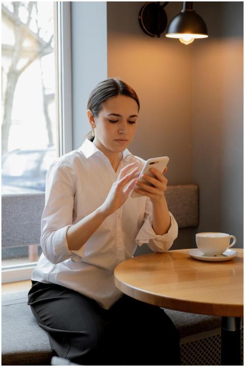 Woman in white shirt using smartphone at a cafe wi