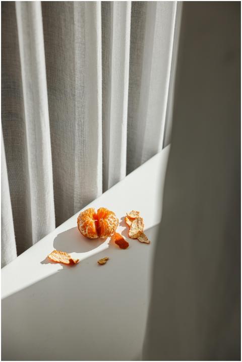 A peeled orange sits on a white surface with natur