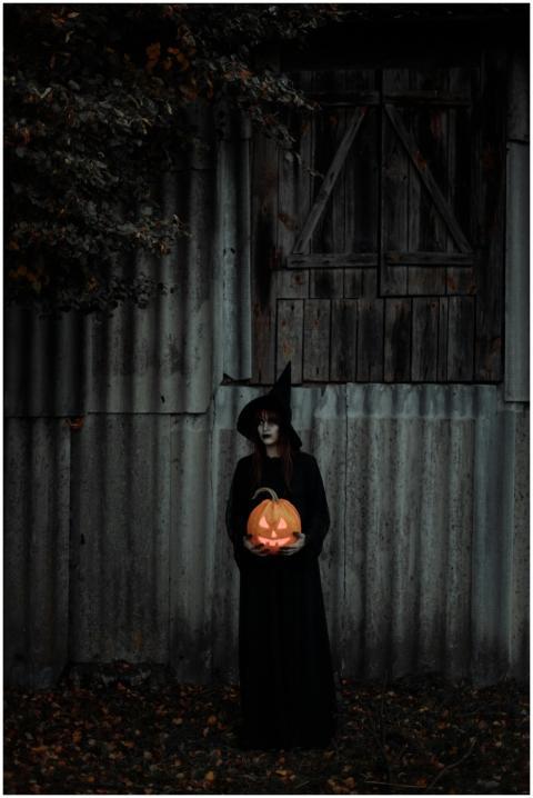 A witch in costume holding a carved pumpkin under