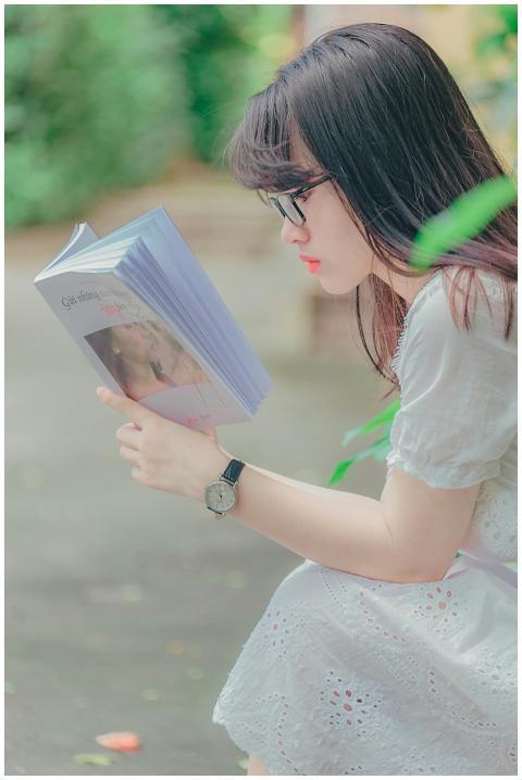 Side view of a young woman reading a book outdoors