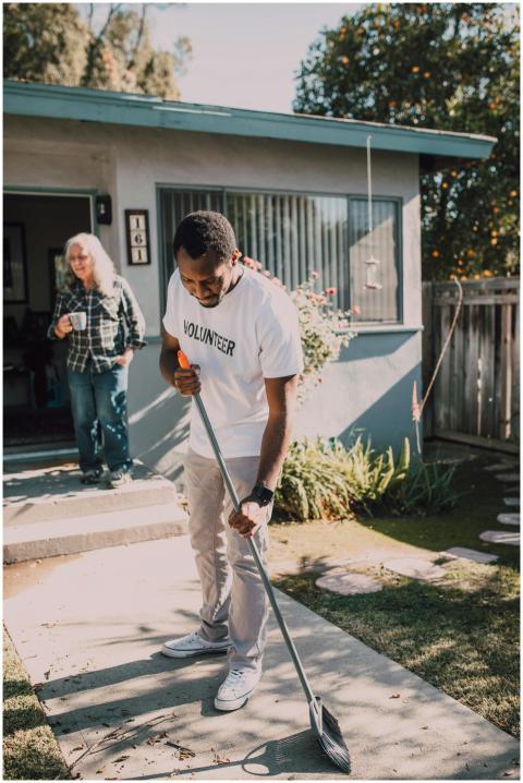 Young volunteer sweeping outdoor yard during a com