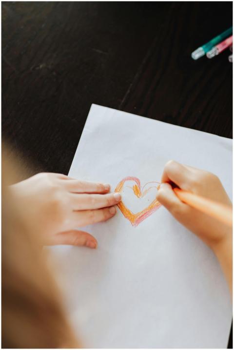 A child draws a colorful heart on white paper usin