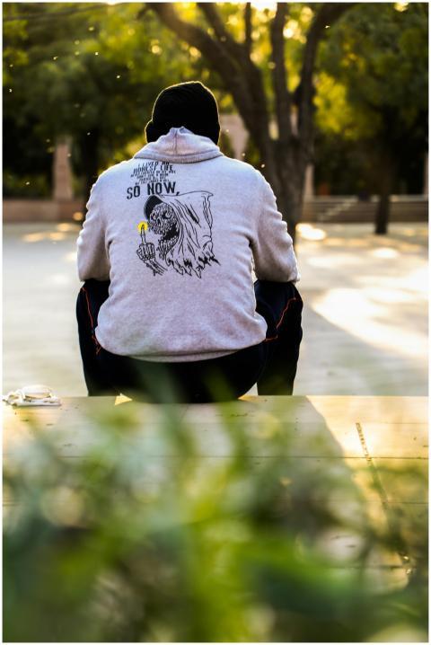 Person wearing a hoodie sitting outdoors in a sunn