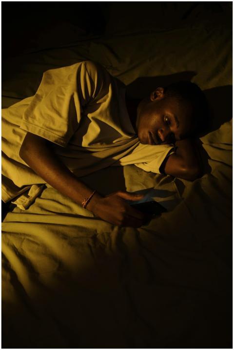 A young man lying in bed at night checking his pho