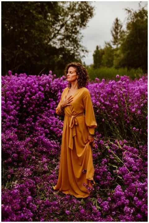 A woman in an orange dress stands meditatively in