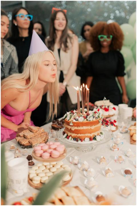 A woman blowing candles on a birthday cake surroun