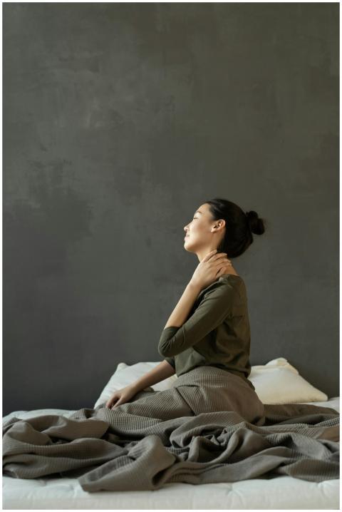 Side view of a woman sitting on a bed indoors, mas