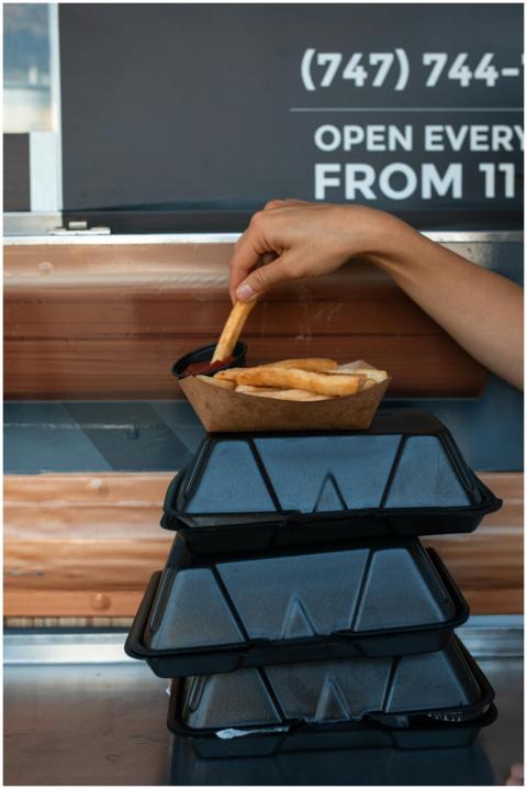 A hand holding a French fry above sauce at a food