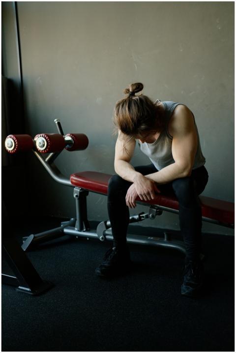 A male bodybuilder resting on a gym bench, looking