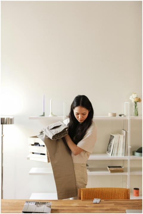 Asian woman tidying indoors, organizing clothes on