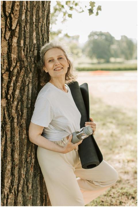 Smiling elderly woman outdoors with yoga mat and w