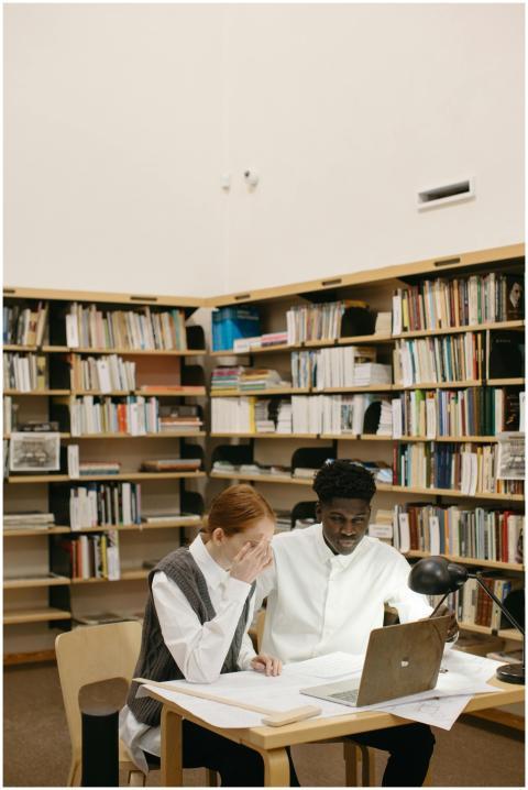 Two students study together at a library desk with