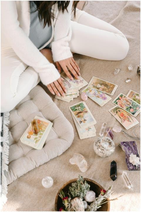 A woman sits cross-legged indoors, handling tarot