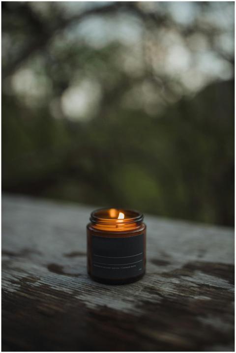 A lit candle in a glass jar sits on a wooden surfa